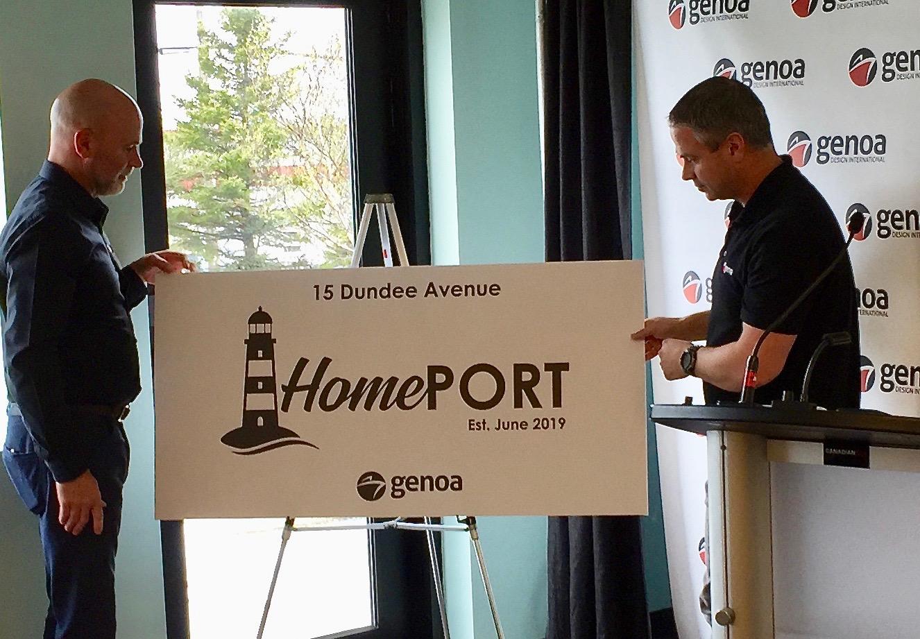 Two individuals stand beside a signboard that reads "15 Dundee Avenue HomePORT Est. June 2019" with a lighthouse symbol, during an indoor event hosted by Genoa Design International.