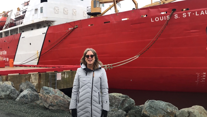 Women in a gray coat standing in front of a large red and white ship, the Louis S. St. Laurent.