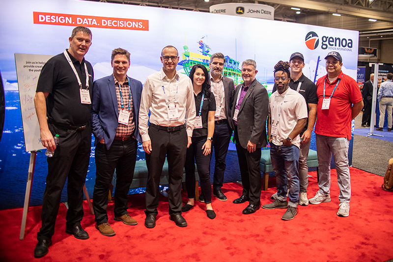 A group of professionals standing in front of a promotional banner reading "DESIGN. DATA. DECISIONS." at a corporate event, banner features an image of a green ship on water, sign for Genoa Design International in the right corner.