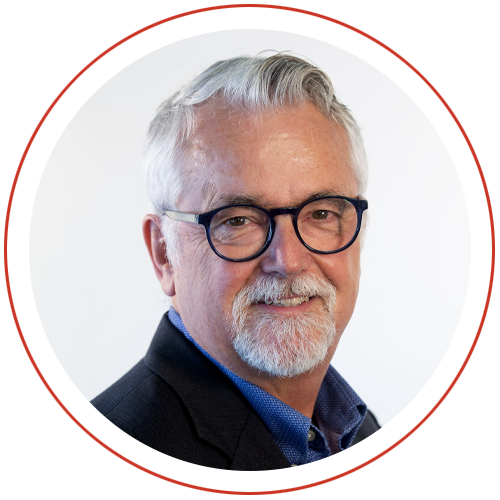 Profile view of a man wearing a dark blazer and blue shirt, set against a white background within a circular border with a thin red outline.