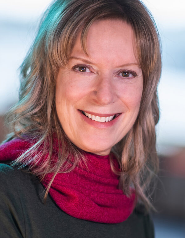 Women wearing a black top and a pink scarf, smiling into the camera, with a blurred background.