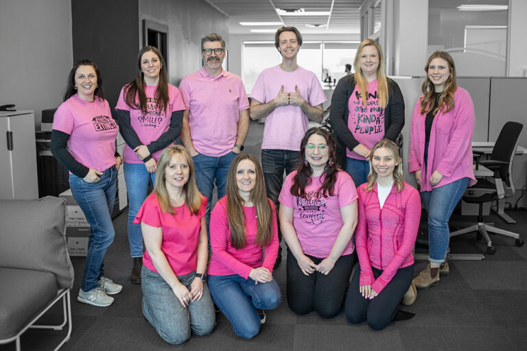 Group of people advocating for community support, wearing pink shirts with various slogans standing and sitting in an office environment