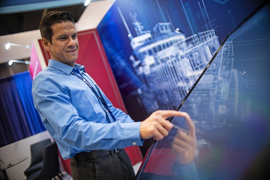 Professional man interacting with a futuristic touchscreen interface at a technology expo, engaging with a digital simulation of a ship.