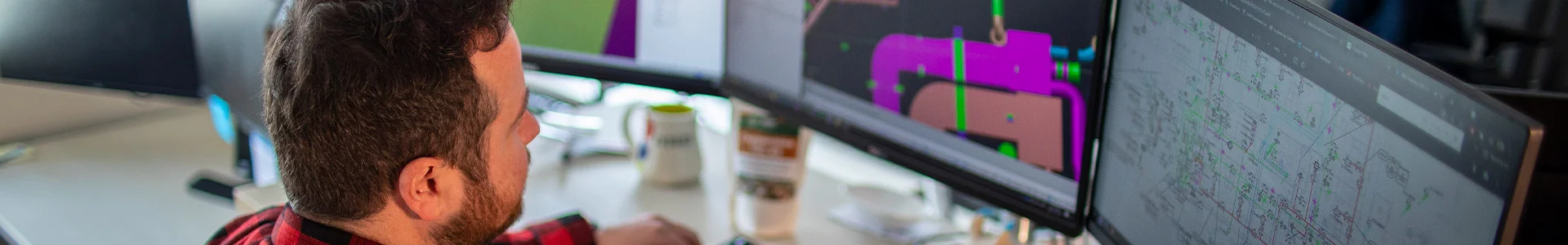 Man analyzing CAD designs on dual monitors in a modern office setting, focusing intently on complex engineering drawings.
